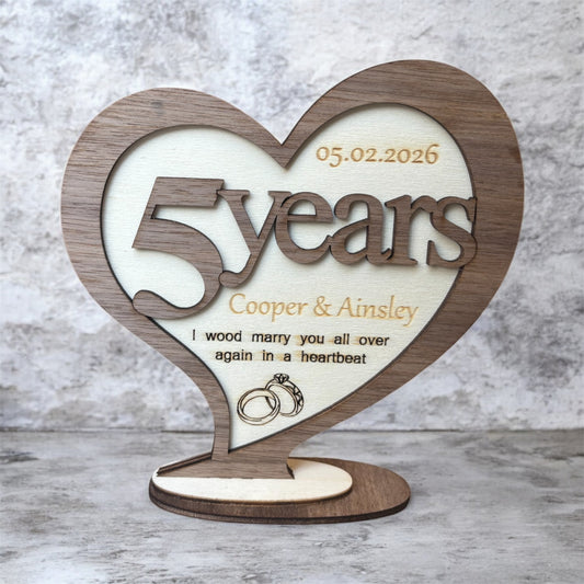A heart-shaped wooden wedding anniversary plaque on a small round base, engraved with '5 years', two names and personalised date. It has the wording "I wood marry you all over again in a heartbeat".